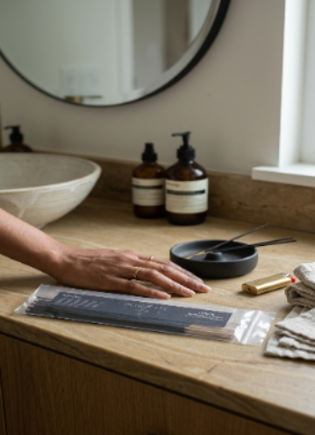 Bathroom counter with skincare products, a bowl, incense and a person's hand.