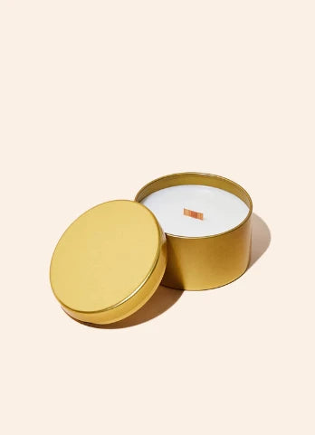 Gold candle tin with a white candle inside on a beige background